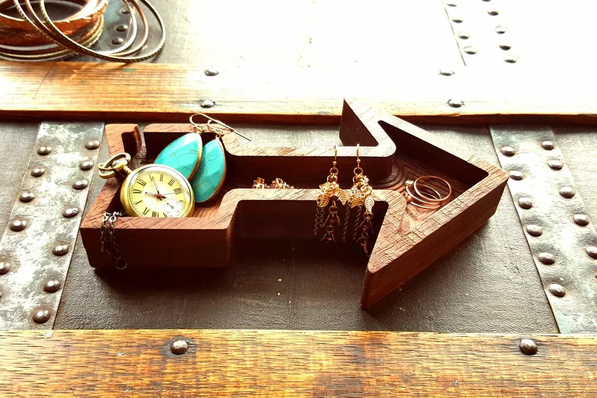A walnut arrow-shaped dish holding jewelry and a pocket watch.