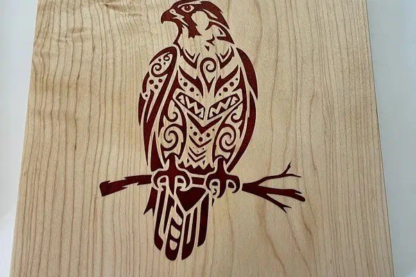 An eagle inlaid in dark padauk into a pale maple panel, cut as a V-carve inlay.