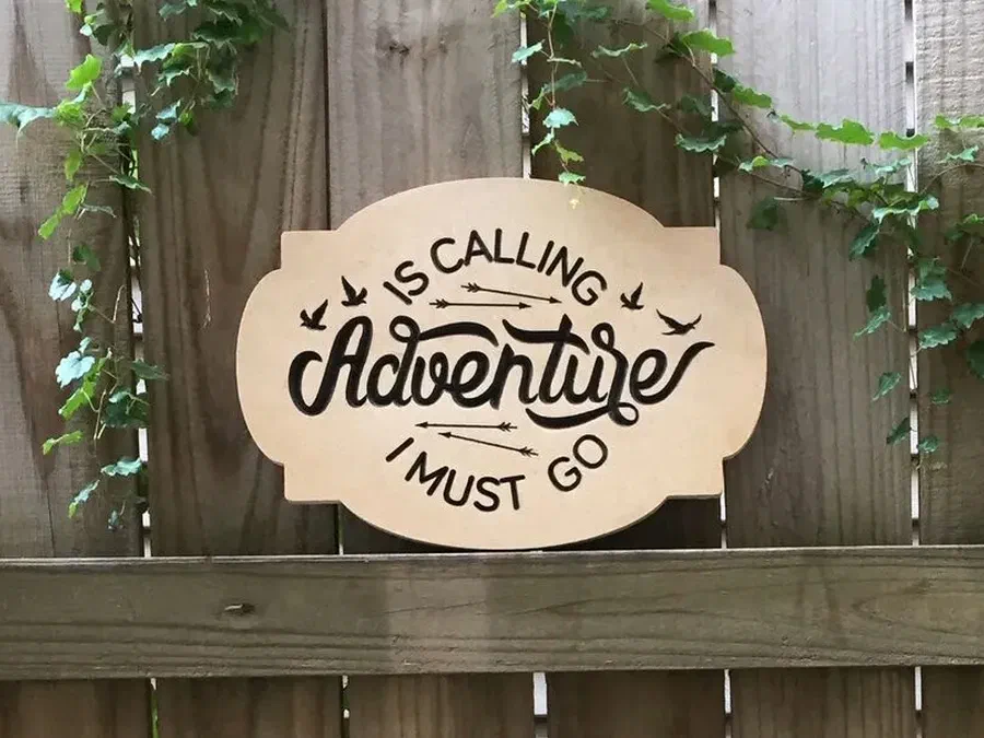 A wooden sign engraved with the phrase Adventure is calling and I must go.