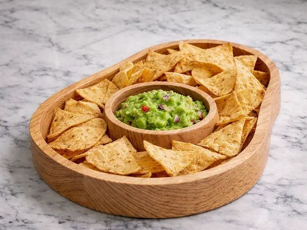A round wooden serving dish holding tortilla chips around a bowl of guacamole.