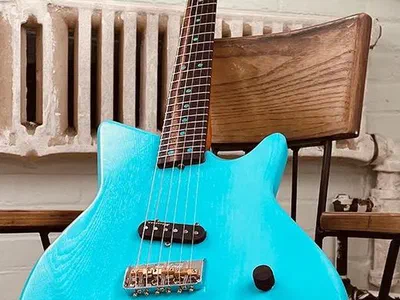 A blue solid body electric guitar with a maple neck, leaning against a chair.
