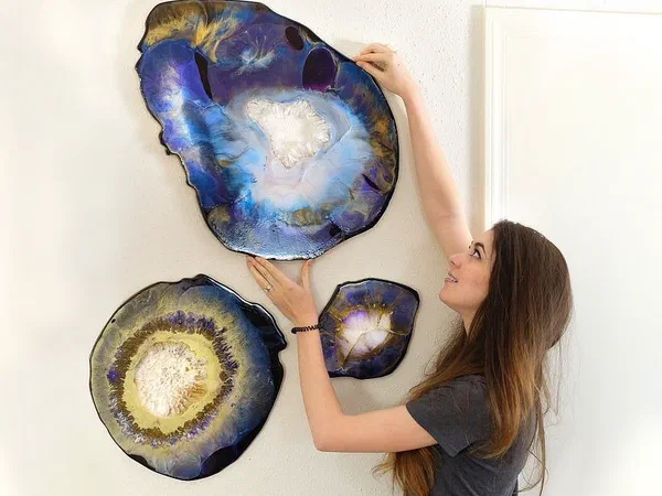 A person hanging three geode-shaped wall panels finished in blue and gold resin.