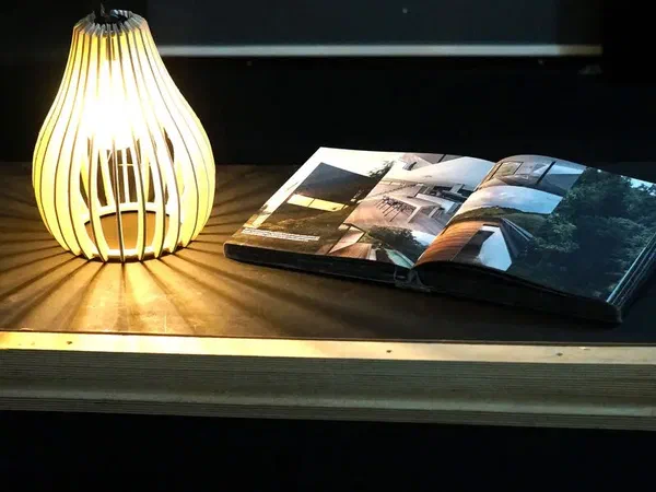 A slatted hanging lamp lighting a magazine on a table in a dark room.