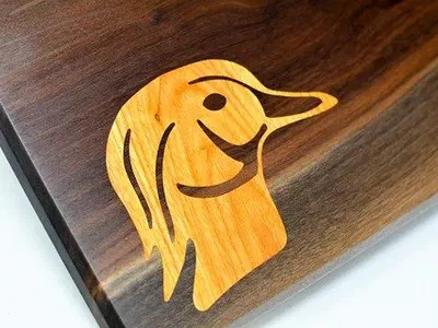 A duck head inlaid in pale wood into a dark live-edge board.
